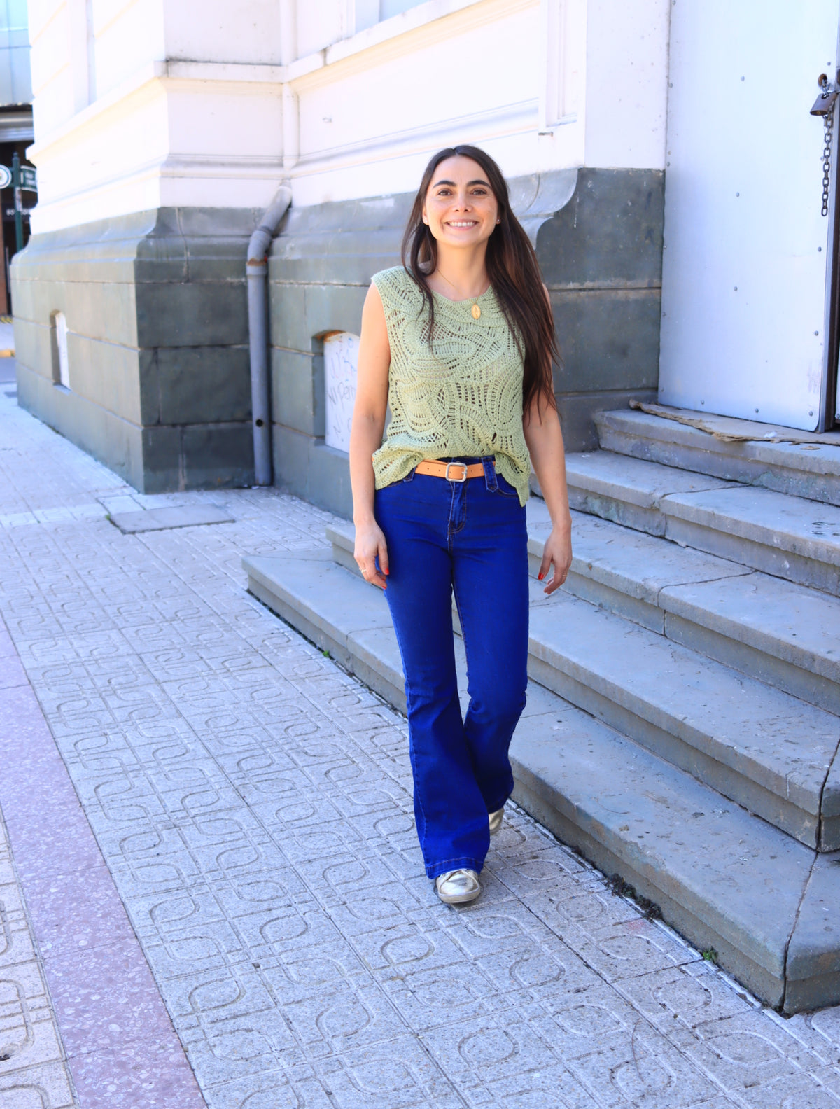 Mujer caminando con jeans flare azul, tejido verde y zapatillas plateadas