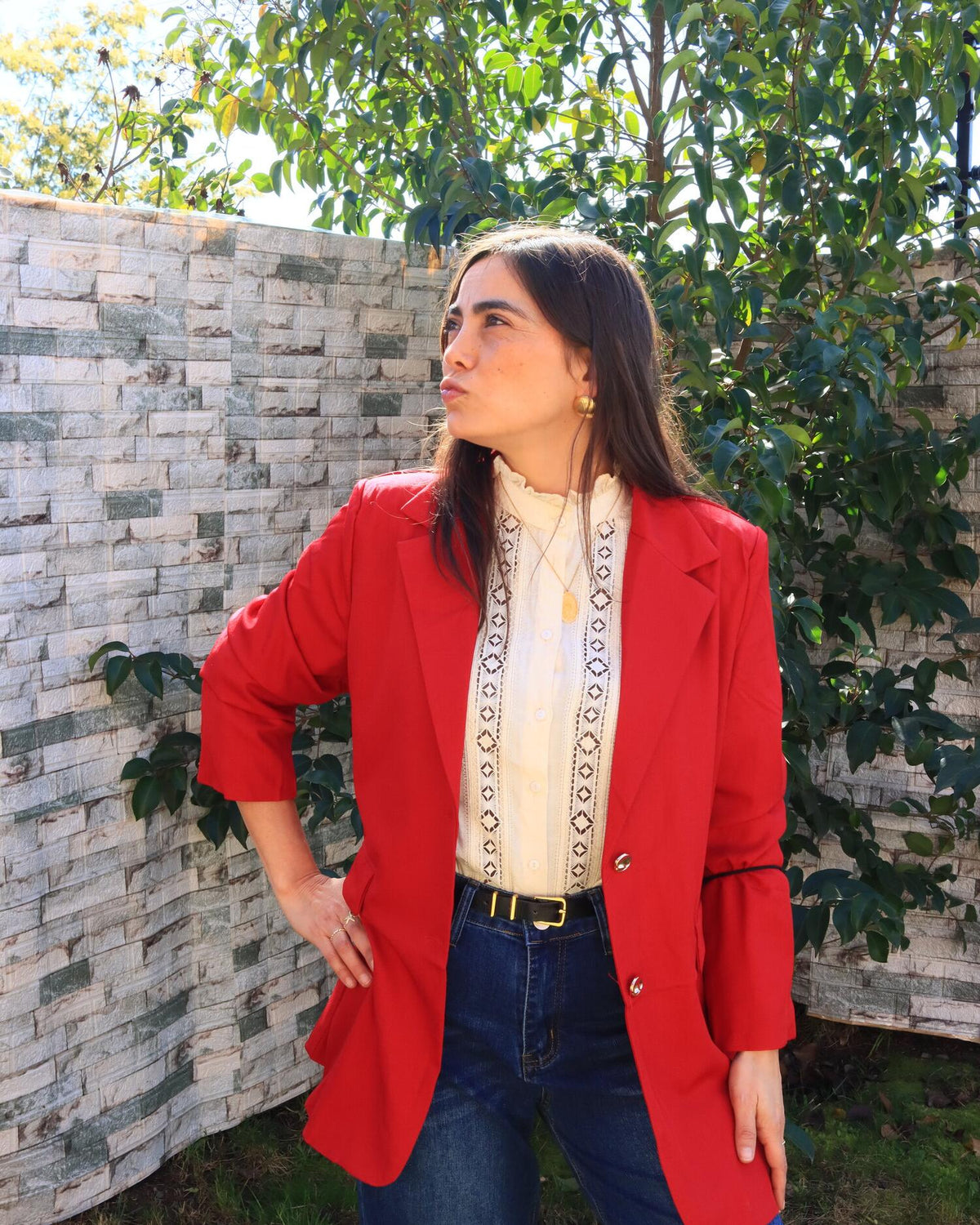 Valeria con blazer rojo y blusa bordada frente a un muro con plantas