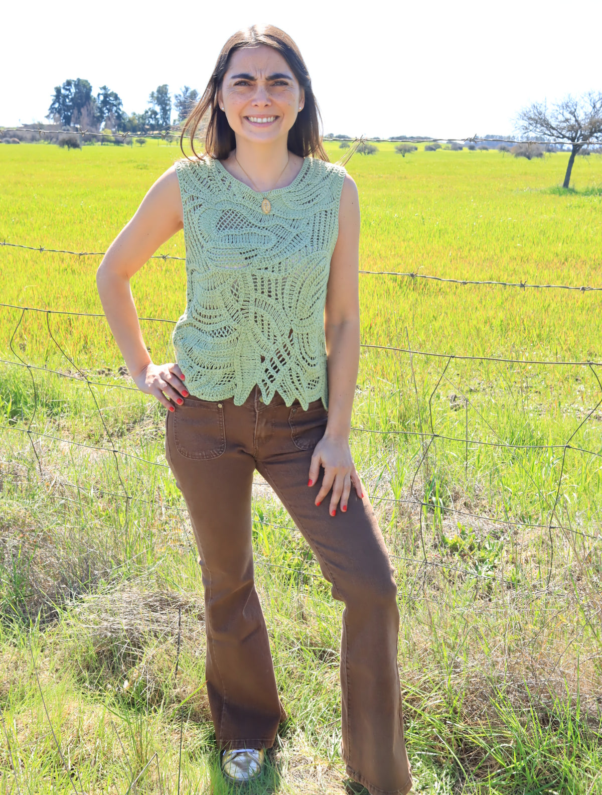 Mujer con jeans marrón de tiro alto y top tejido verde, de cuerpo entero en un campo